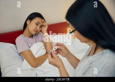 Caring mother measuring body temperature of her ill adult daughter Stock Photo