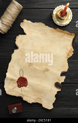 Sheet of old parchment paper with wax stamp, twine and candle on black wooden table, top view Stock Photo