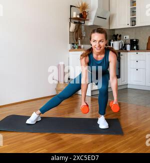 Motivated woman wearing sportswear doing workout with dumbbells at home. Sporty and healthy lifestyle. Stock Photo