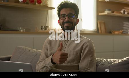 Smiling Arabian muslim man freelancer working from home use laptop technology happy businessman guy on couch in kitchen satisfied online order Stock Photo