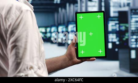 Elderly repairman in data center using mockup tablet to monitor energy efficient servers using renewable sources employed to minimize consumption and reduce overall facility carbon footprint Stock Photo