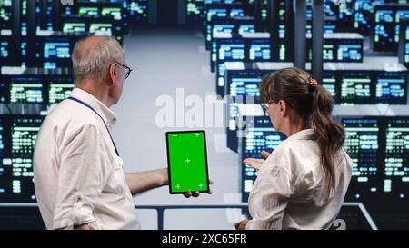 Precise managers looking around high tech data center, using mockup laptop to crosscheck disaster recovery plan and assess servers rigs in need of replacement, preventing complications Stock Photo