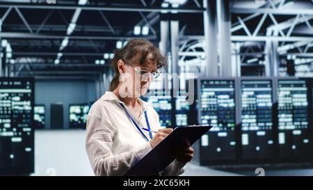 Aged IT admin in modern server room holding clipboard during data center maintenance, crossing off completed tasks. Trained specialist in high tech workspace finishing checkup on equipment Stock Photo