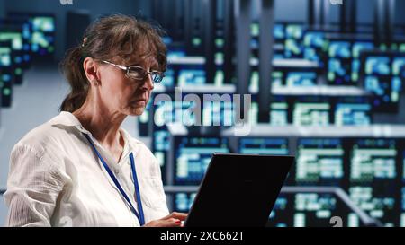 Elderly engineer in data center equipped to handle modern computing requirements, doing regular upgrades to components, increasing processing power, storage capacity and general efficiency Stock Photo