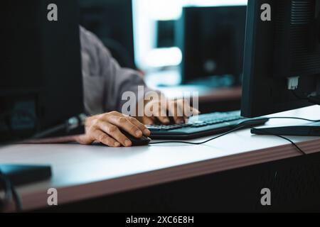 Hands typing on a keyboard and using a mouse at a busy training center, focusing on repairing hardware and troubleshooting it issues Stock Photo