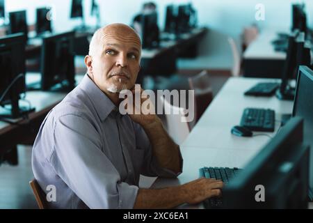 Focused mature man at desk, coding and problem solving on computer in tech filled office. Professional programmer seeking innovative solutions Stock Photo