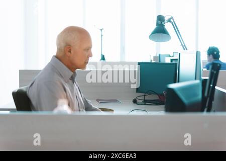 Senior it specialist deeply focused on computer work in a modern office space. Bright natural light highlights his expertise in technology Stock Photo