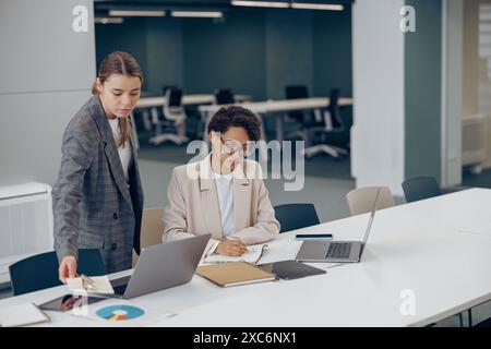 Focused business woman work together with documents and making notes while use laptop at the office Stock Photo