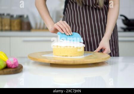 Closeup hand holding plastic cake cream spatula, spread the top of the cake with white cream, creating a decorative pattern on the top of a round cake Stock Photo