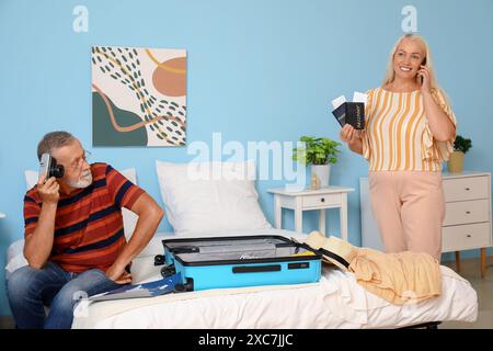 Senior couple with camera, passports and tickets packing suitcase on bed at home and talking by mobile phone Stock Photo