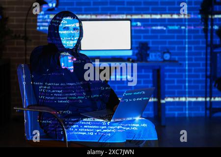 Hacker with laptop and projection of programming code pointing at something in dark room Stock Photo