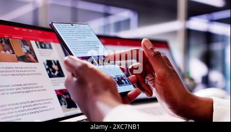 African American Woman Reading Online News on Smartphone and Laptop: Keeping Up with the Latest Headlines on the Go. Stock Photo