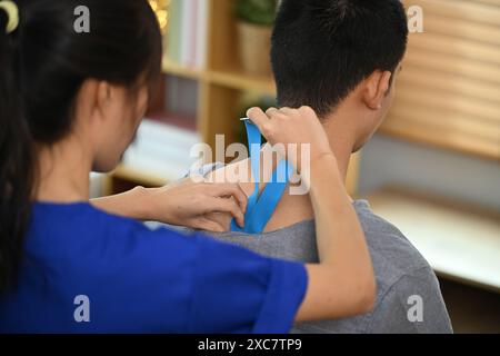 Physical therapist placing Kinesio tape on injured patient shoulder. Kinesiology and rehabilitation concept Stock Photo