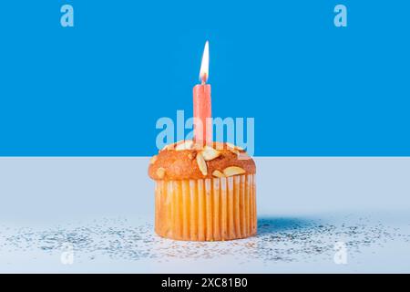 Birthday cupcake with glowing candles on white table with blue background Stock Photo