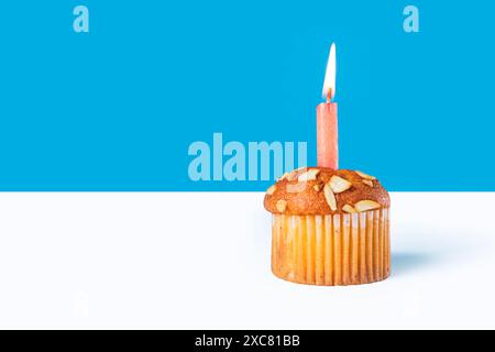 Birthday cupcake with glowing candles on white table with blue background Stock Photo