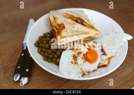 breakfast scrambled eggs hot sandwich with ham and cheese, green peas, legumes on plate Stock Photo
