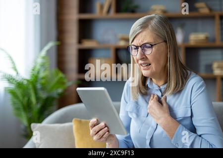 Elderly woman having a virtual medical consultation on a tablet, expressing concern and pain. Online health examination and patient care. Stock Photo