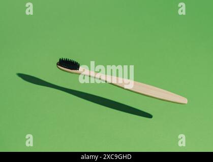 Organic bamboo toothbrush on green background with sun shadow. Minimal dental concept. Creative eco friendly, biodegradable and wooden toothbrush. Stock Photo