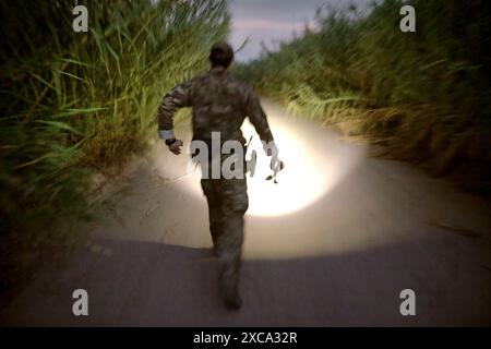 After determining from reading 'sign' that and illegal alien who had just crossed the Rio Grande had already donned clothing and shoes and made a running stride towards a nearby highway, a U.S. Border Patrol Search, Trauma, and Rescue (BORSTAR) agent picks up his pace in the pursuit near Eagle Pass, Texas, June 20, 2019. As Border Patrol agents are tasked with processing and intake responsibilities presented by the recent surge in migrant arrivals at the border, members of BORSTAR have been assisting in pursuing illegal aliens afield. CBP photo by Glenn Fawcett Stock Photo