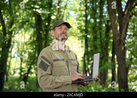 Forester with laptop examining plants in forest Stock Photo