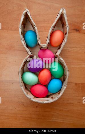 brightly colored hard boiled Easter eggs in a bunny shaped basket on a wooden table Stock Photo