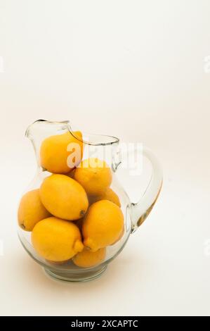 A clear glass pitcher full of whole fresh lemons on a white background Stock Photo