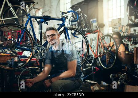Mechanic, portrait and working at startup bicycle repair shop or maintenance garage. Bike, mature man and service with a professional handyman for Stock Photo