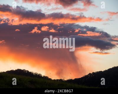 Dramatic weather, pink orange grey storm clouds cell, brightly back lit from the sun shining, perhaps raining in the distance, Australia Stock Photo