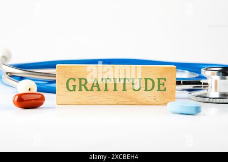 Top view of words GRATITUDE written on a wooden bar in front of a stethoscope next to pills, vitamins Stock Photo