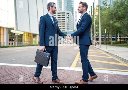 Businessmen in suit shaking hands outdoors. Handshake between two businessmen. wo business men had business contacts. Business men have a meeting Stock Photo