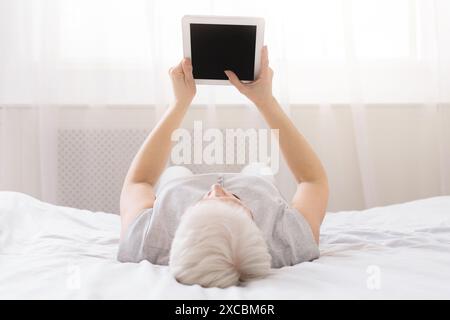 Person Laying on Bed With Tablet with Blank Screen Stock Photo