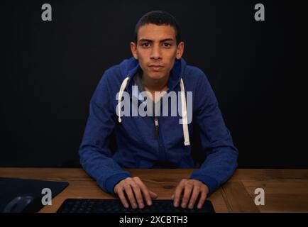Coding, portrait and man typing on desk, working on assignment for gamer. Black background, programming and online development in home, serious on Stock Photo