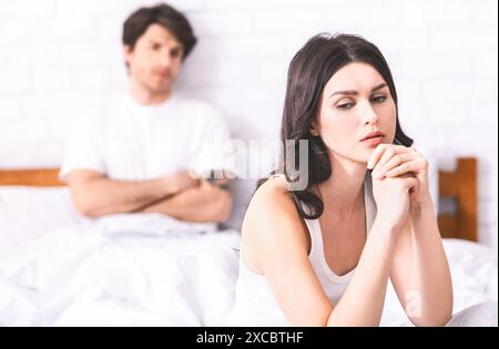 Sad Woman Sitting on Bed While Man Stands in Background Stock Photo
