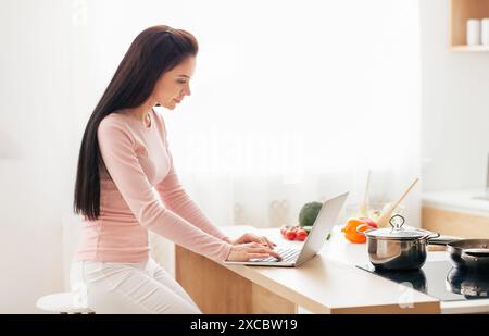 Woman Sitting at Kitchen Counter Using Laptop Computer Stock Photo