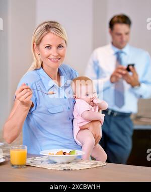 Mother, healthy breakfast and baby in home while multitasking and sitting at kitchen table. Working father, woman and child in family house to eat Stock Photo