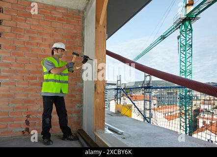 Mason by slashing the wall with hammer and chisel, Bricklayer with personal protective equipment, PPE, Apartment Building under construction, Donostia Stock Photo