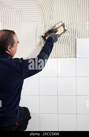 Preparing wall with glue mortar before tiling using a serrated plastering trowel, new homes under construction, construction site Stock Photo