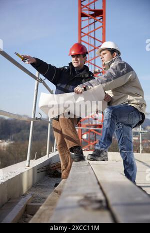 Architect and construction worker looking at blueprints, personal protective equipment, housing construction Stock Photo