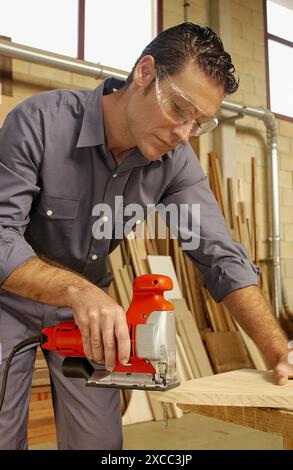Carpenter cutting wood plank with fretsaw Stock Photo