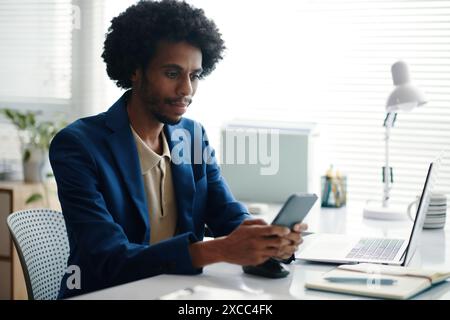 Serious entrepreneur checking notifications on smartphone when working in office Stock Photo