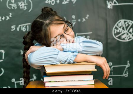 schoolgirl with glasses fell asleep on a pile of books while sitting at the table. Stock Photo