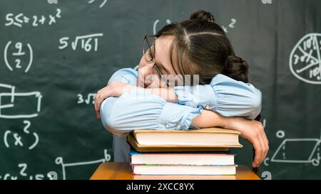 A schoolgirl with glasses fell asleep pile of books while sitting at the table. Stock Photo