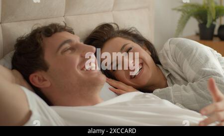 Caucasian couple man woman lying on bed home discussing plans chatting talking laughing happiness girlfriend boyfriend honeymoon romance togetherness Stock Photo