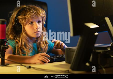 Child plays a video game on the pc computer screen. Portrait of cute child while typing on keyboard. Gamer play computer games. Neon lighting. Stock Photo