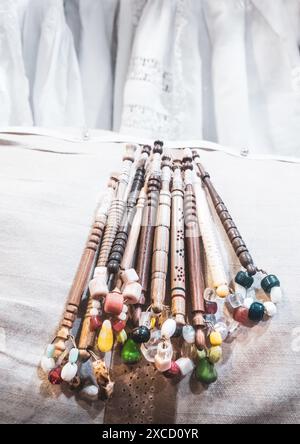 A close-up of traditional wooden bobbins with colorful beads used for lace making on a fabric background. Stock Photo