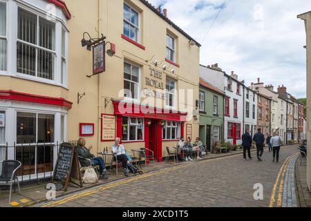 Staithes, a pretty fishing village on the North Yorkshire coast, England UK, with winding cobbled streets. People sitting outside The Royal George pub Stock Photo