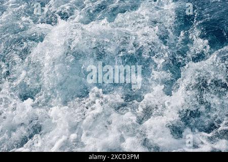 Sea waves, bubbles and white foam over the blue sea formed by the motor of a powerboat. Stock Photo