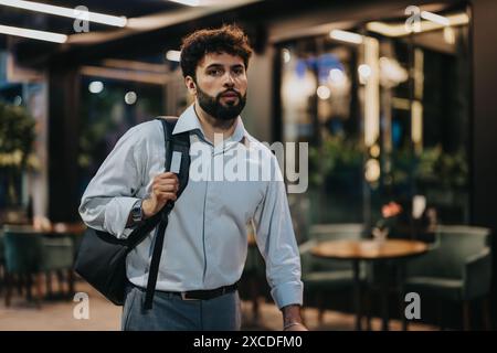 Businessman walking through modern office lobby with bag on shoulder, looking focused Stock Photo