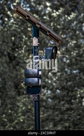 License plate recognition camera blends in with the background. The camera, mounted on a black pole, captures license plate data of passing vehicles. Stock Photo