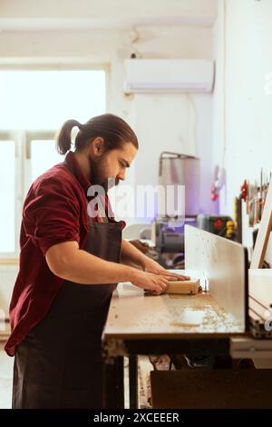 CNC machinist operating wood shaper in assembly shop, creating intricate designs with precision. Woodworking specialist uses spindle moulder to shape and mold timber pieces Stock Photo